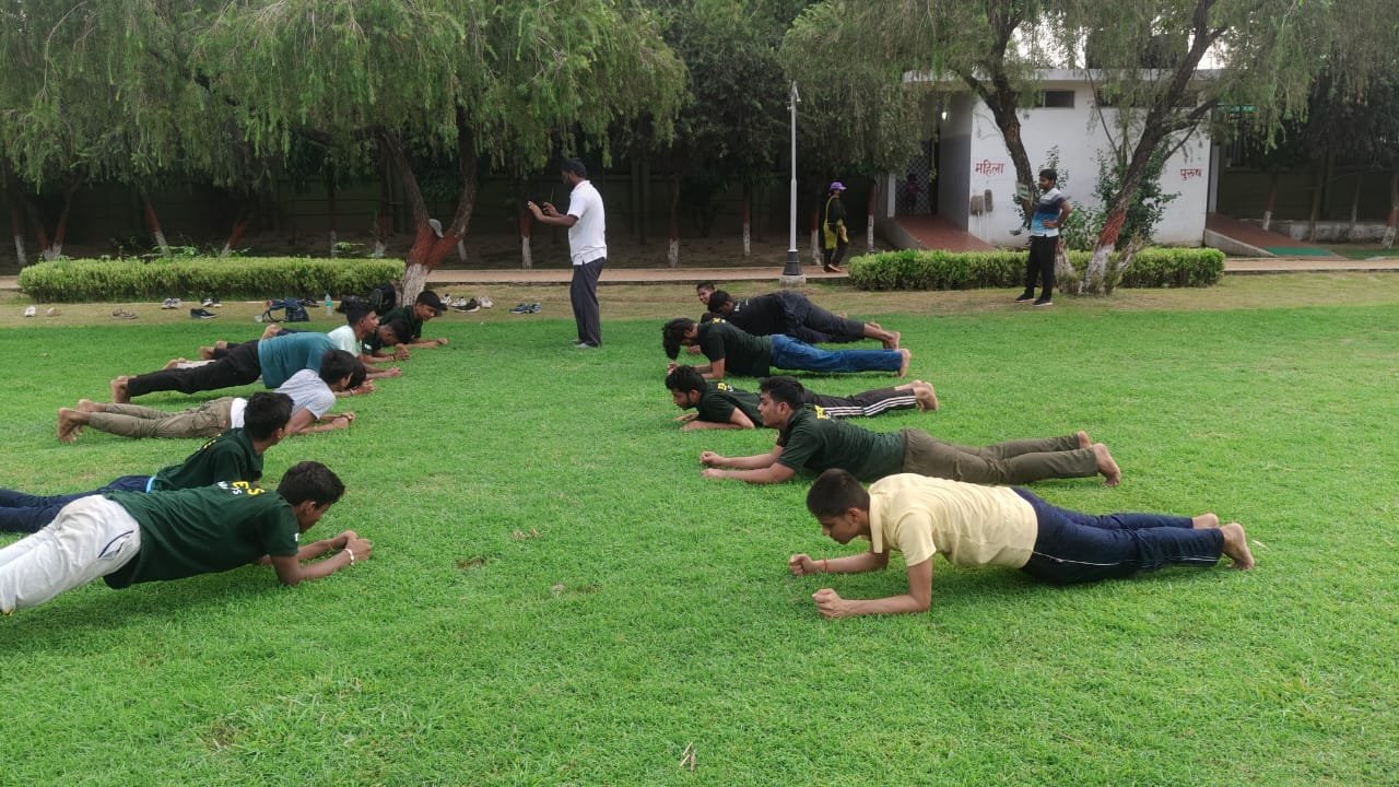 Students practising push-ups in two rows on a grassy training ground.